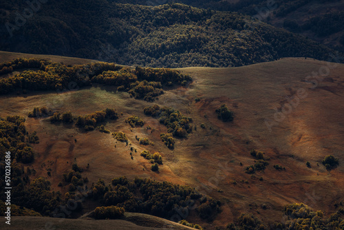 Photo of a scenic view of the hill with forest and trees under sunlight and clouds shadows from the plateau Bermamyt. There are trees in autumn colors on the top of the hills and background. 