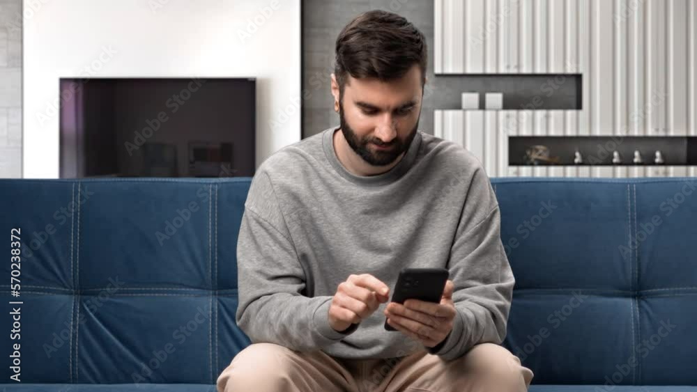 Smiling man use smartphone dating app chatting internet browsing relaxing on couch at home apartment Smiling man use smartphone dating app chatting internet browsing relaxing on couch at home apartment