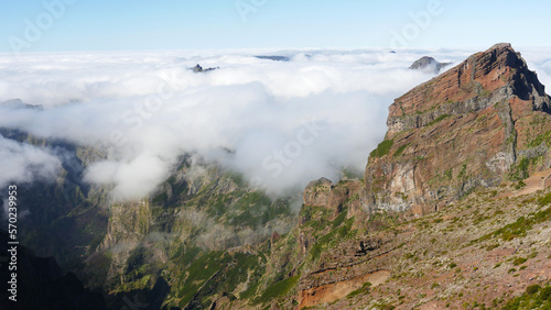Above the clouds in Madeira, with tree covered hills shing green in the sunshine. Blue sky above.