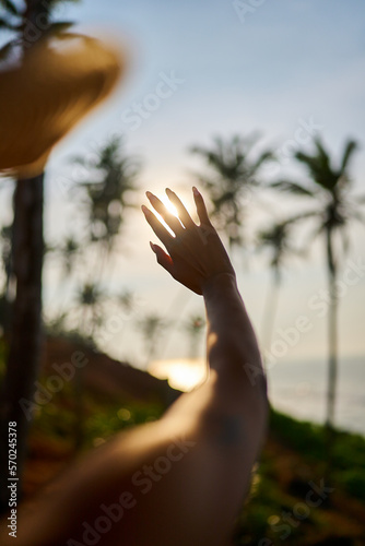 Silhouette of delicate feminine hand covering the sun. Black woman covers sun with hand and fingers closeup shot from back. African young woman stretches arm and fingers to sun and plays with light