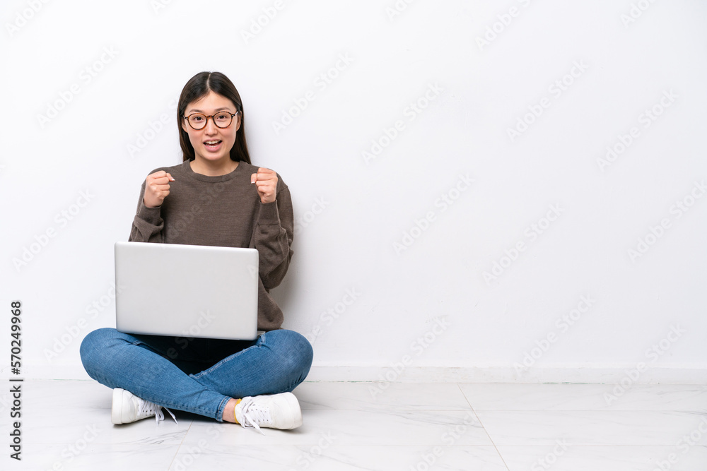 Young woman with a laptop sitting on the floor celebrating a victory in winner position Young woman with a laptop sitting on the floor celebrating a victory in winner position