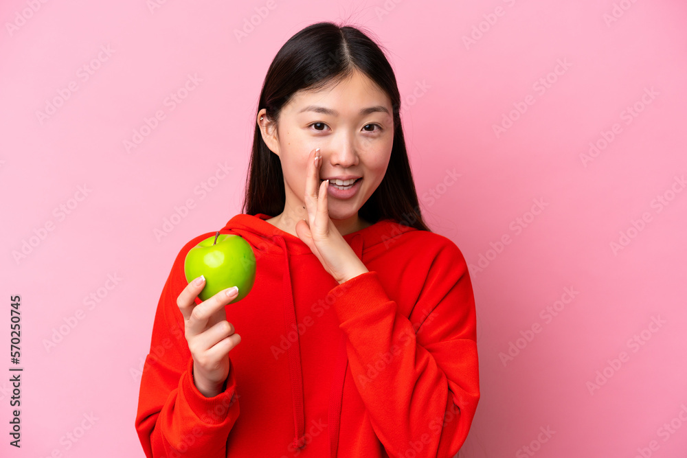 Young Chinese woman with an apple isolated on pink background whispering something Young Chinese woman with an apple isolated on pink background whispering something