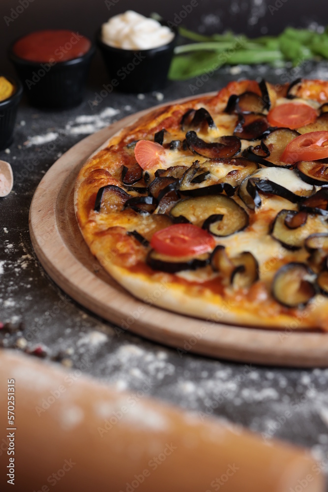 a pizza with mushrooms, eggplants, aubergine and tomatoes on a wooden board on a table with other ingredients around it a pizza with mushrooms, eggplants, aubergine and tomatoes on a wooden board on a table with other ingredients around it