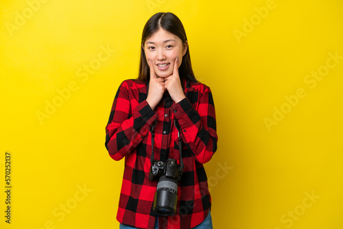 Young photographer Chinese woman isolated on yellow background smiling with a happy and pleasant expression © luismolinero