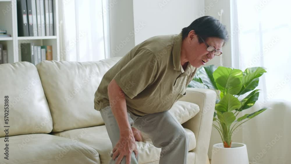 Asian senior man standing up then suffering from knee pain at home Asian senior man standing up then suffering from knee pain at home