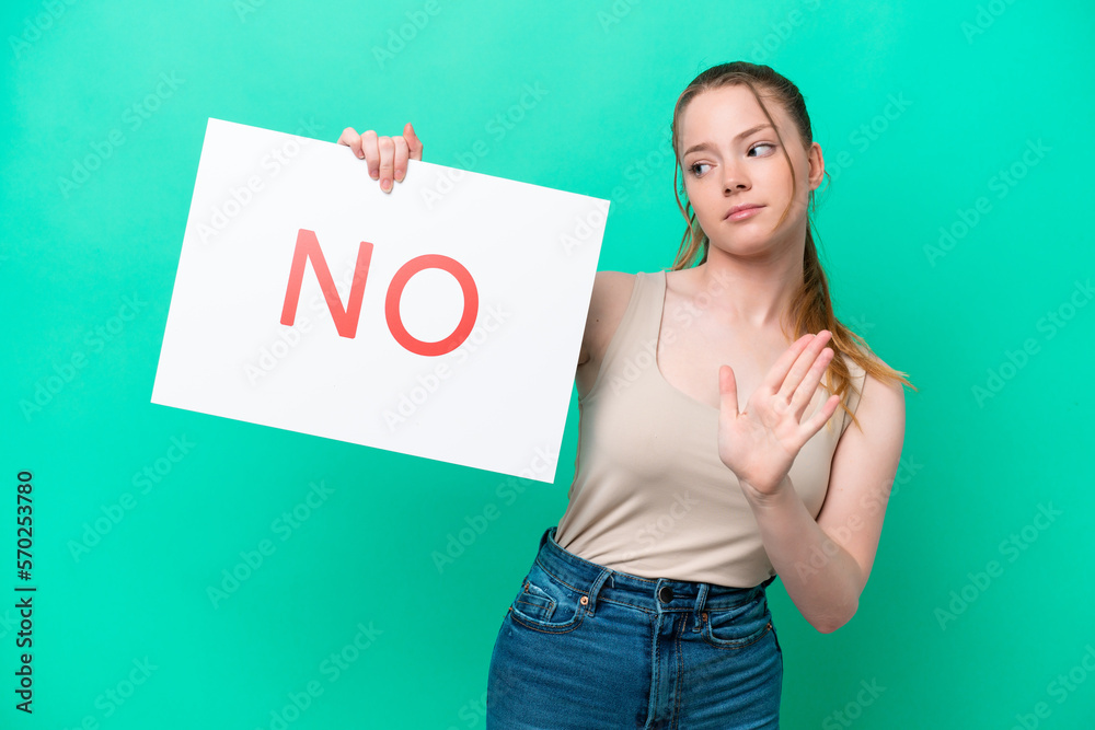 Young caucasian woman isolated on green background holding a placard with text NO and doing stop sign Young caucasian woman isolated on green background holding a placard with text NO and doing stop sign