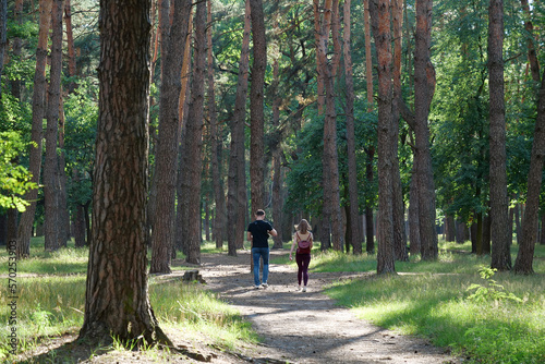 Man and woman walk among coniferous trees in beautiful summer forest