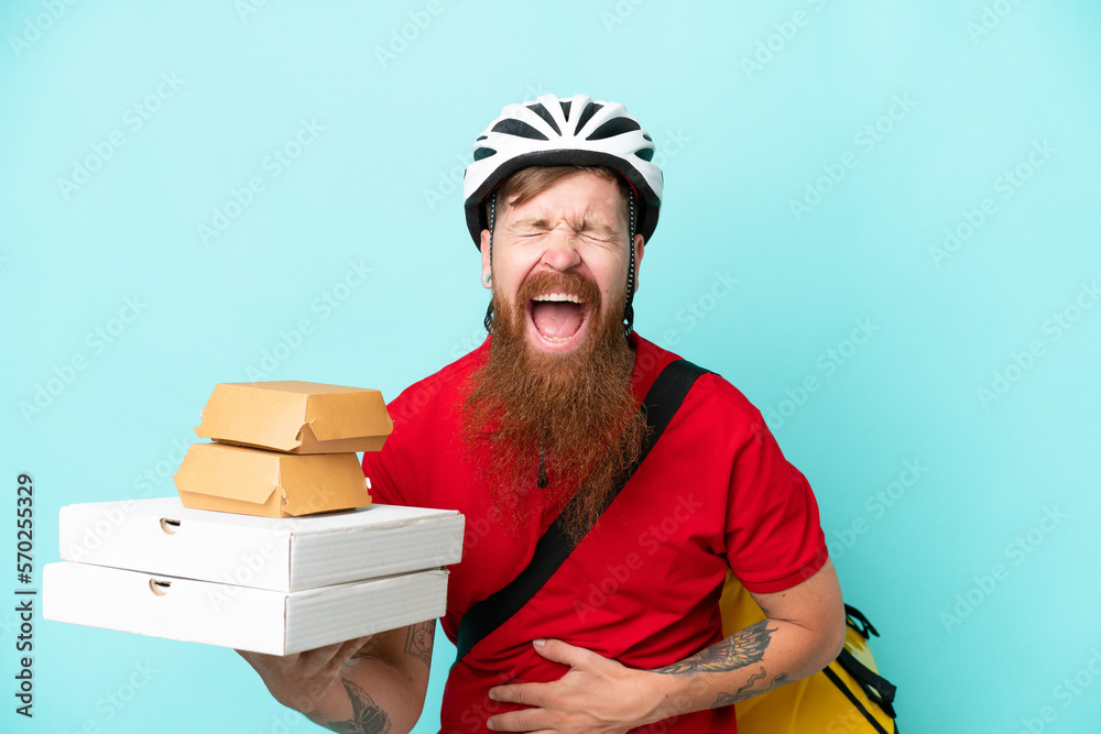 Delivery man holding pizzas and burgers isolated on blue background smiling a lot