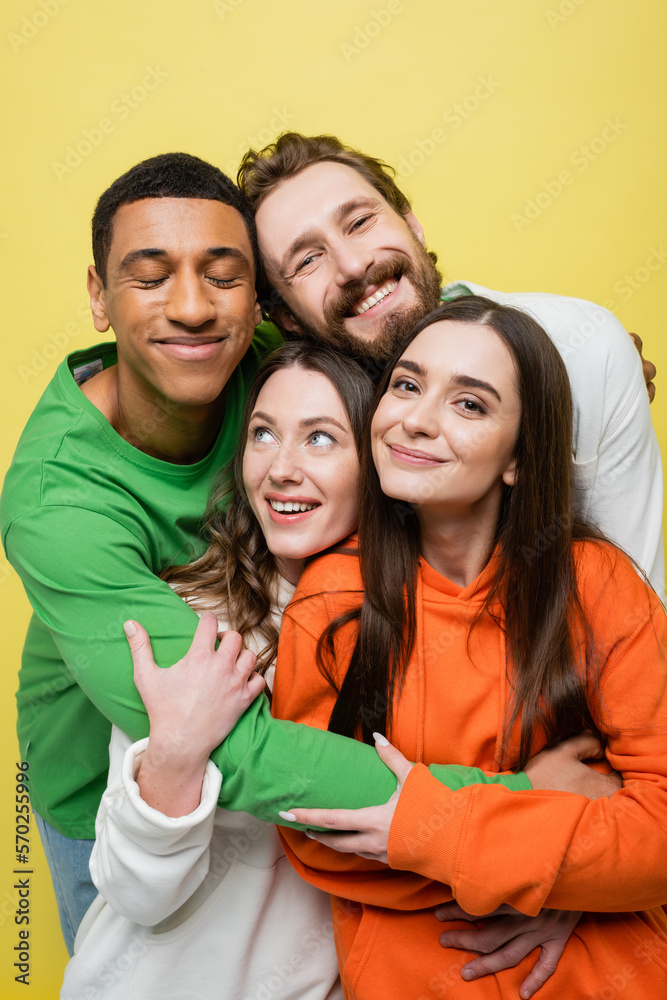 Positive multiethnic people hugging isolated on yellow