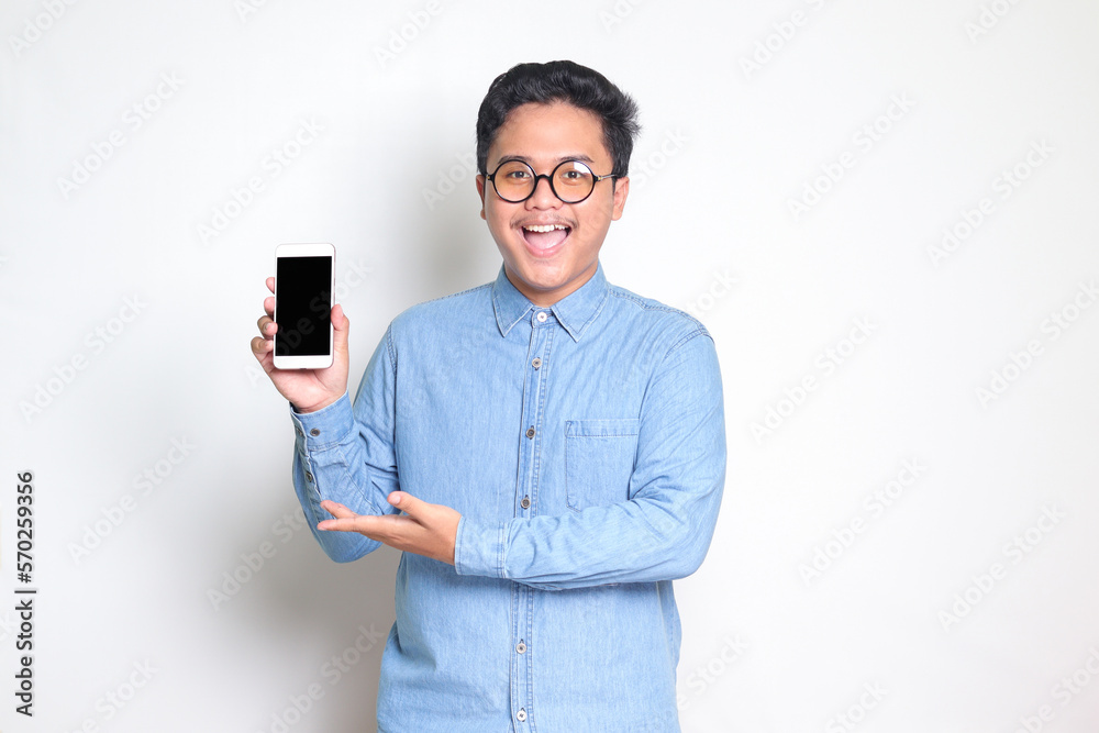 Portrait of excited Asian man in blue shirt showing and presenting blank screen mobile phone. Advertising concept. Isolated image on white background