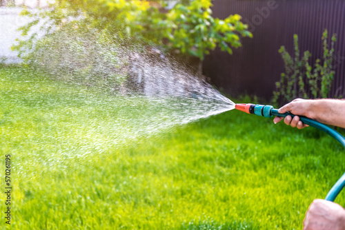 Gardener's hand holds a hose with a sprayer and watering grass
