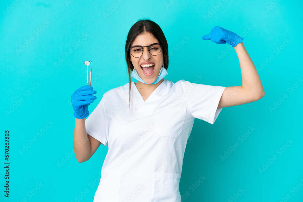 Young caucasian dentist woman holding tools isolated on blue background doing strong gesture Young caucasian dentist woman holding tools isolated on blue background doing strong gesture
