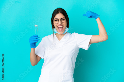 Young caucasian dentist woman holding tools isolated on blue background doing strong gesture