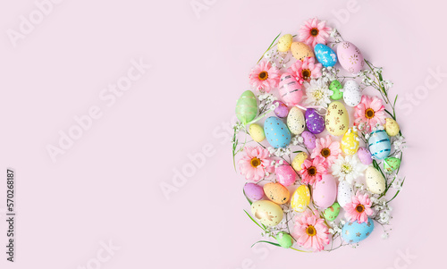 Easter egg shape with flowers and decorated eggs on pink background with copy space. Creative layout concept for greetings card for the holiday season.