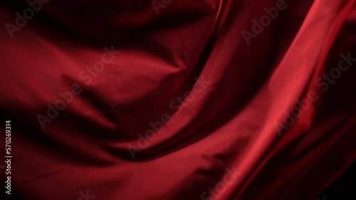 The chic and elegant texture of the moving folds of light red fabric on a black background under dramatic lighting. Slow Motion 200 FPS