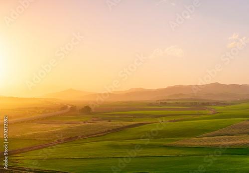 countryside sunset in green hills of spring fields with old castle farm and mountains on background of evening landscape