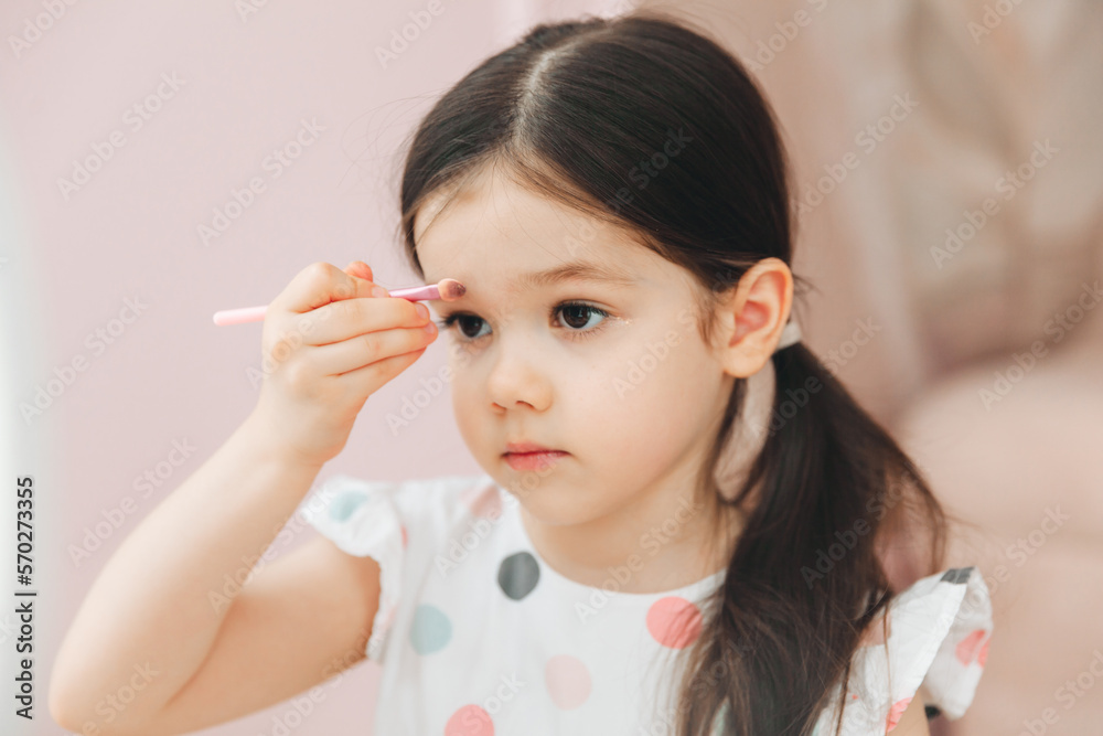 a beautiful little girl in the mirror preening. a little girl is sitting at a children's table and is wearing children's cosmetics. a beautiful little girl in the mirror preening. a little girl is sitting at a children's table and is wearing children's cosmetics.