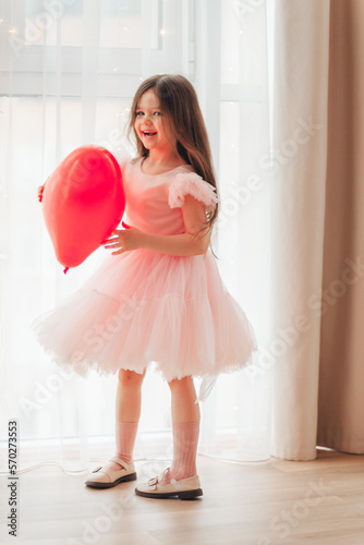 valentine's day baby. A little girl in a red dress holds a large ball in the shape of a heart