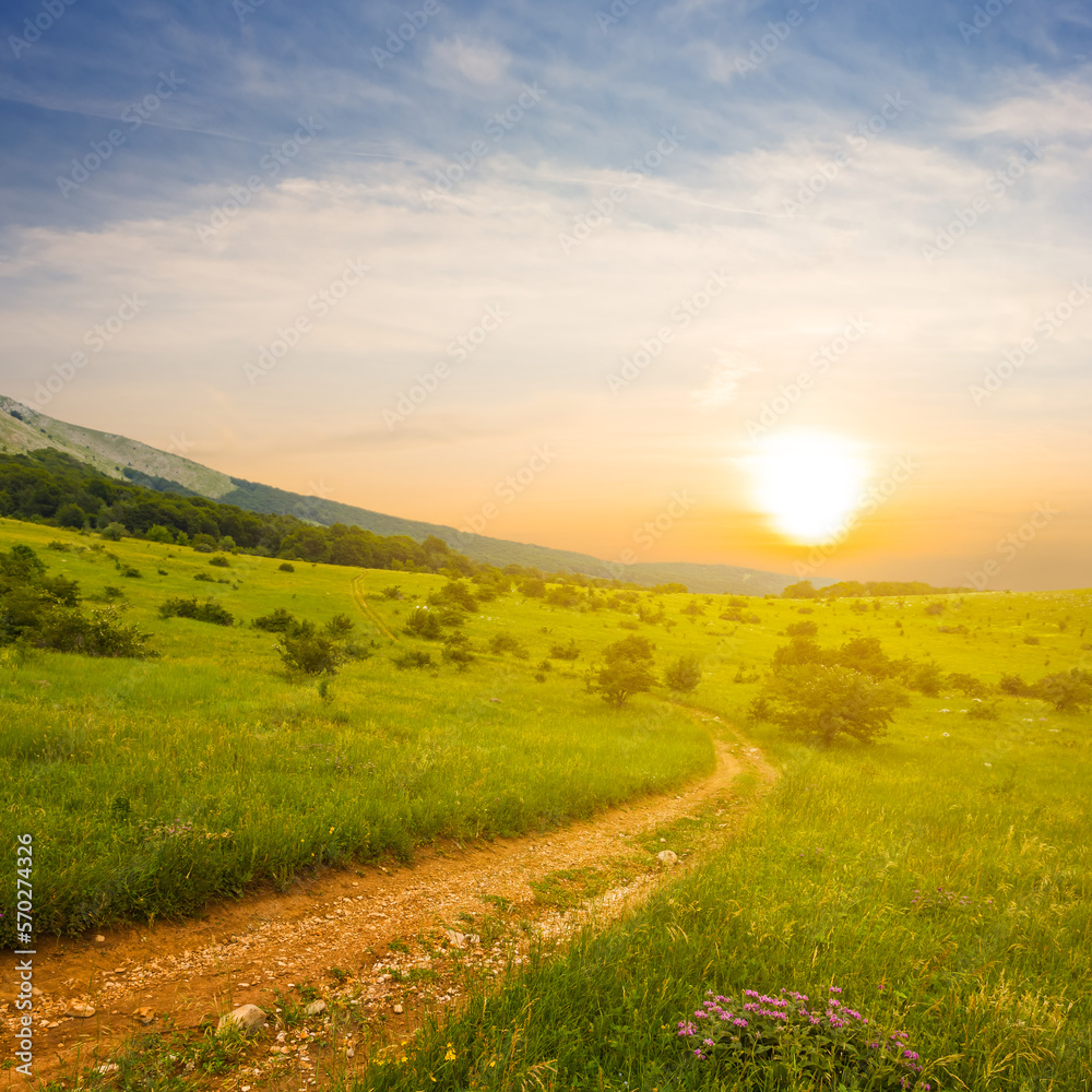 Obraz premium ground road among green mountain valley at the sunset