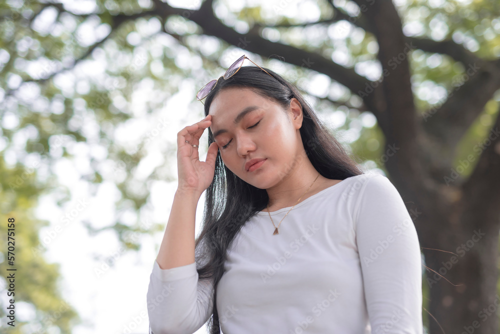 A young lady standing outside the park closes her eyes and touches the temple of her head as she experiences headache. A young lady standing outside the park closes her eyes and touches the temple of her head as she experiences headache.