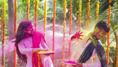 Happy excited couple playing holi together at festival ceremony - concept of playful or fun, togetherness and colourful Indian tradition