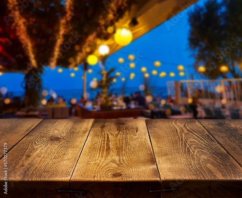 Festive background. Evening. Night. Abstract background. An empty wooden countertop against the background of a restaurant by the sea. Bokeh, garlands, blurred lights. Rest. Outdoors.