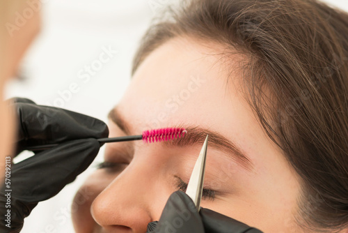 Young woman undergoing eyebrow correction procedure in beauty salon, closeup. Brow comb,