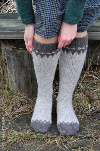 The girl fixes knitted high socks with a pattern.  Front view.