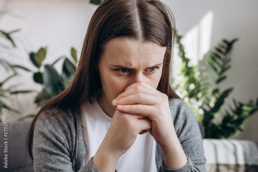 Close up of stressful sad young caucasian woman sitting alone on couch in living room covering face with hands. Emotional brunette female 20s feeling upset and unhappy at home. Depression concept Close up of stressful sad young caucasian woman sitting alone on couch in living room covering face with hands. Emotional brunette female 20s feeling upset and unhappy at home. Depression concept