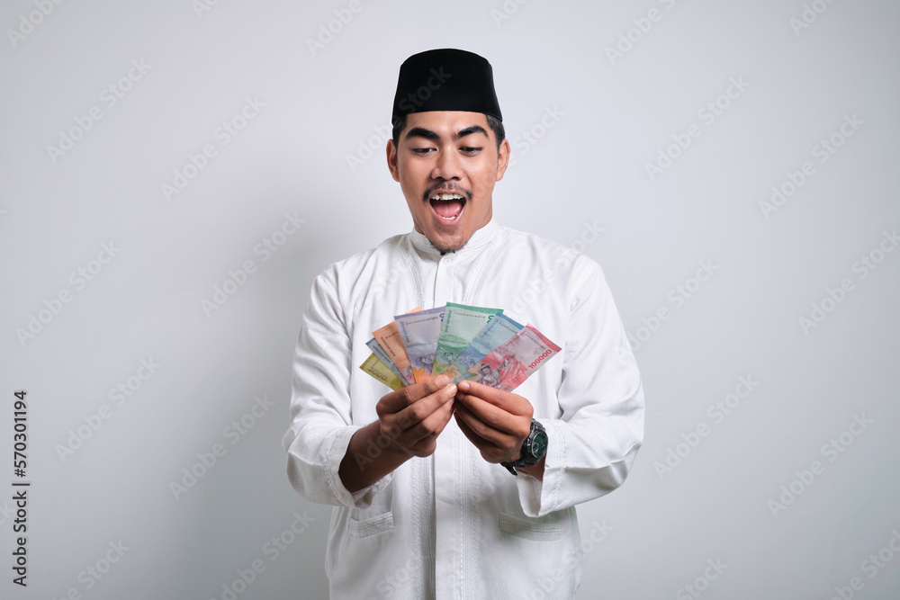 Smiling asian muslim man in white clothes holding rupiah money paper Smiling asian muslim man in white clothes holding rupiah money paper
