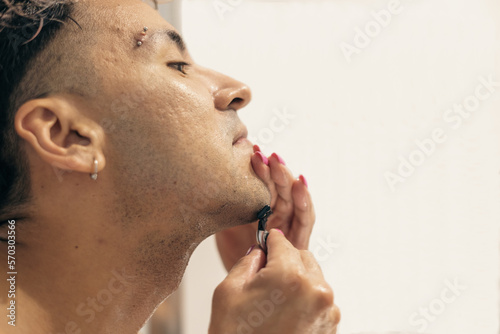Non binary person shaving his beard before applying make-up