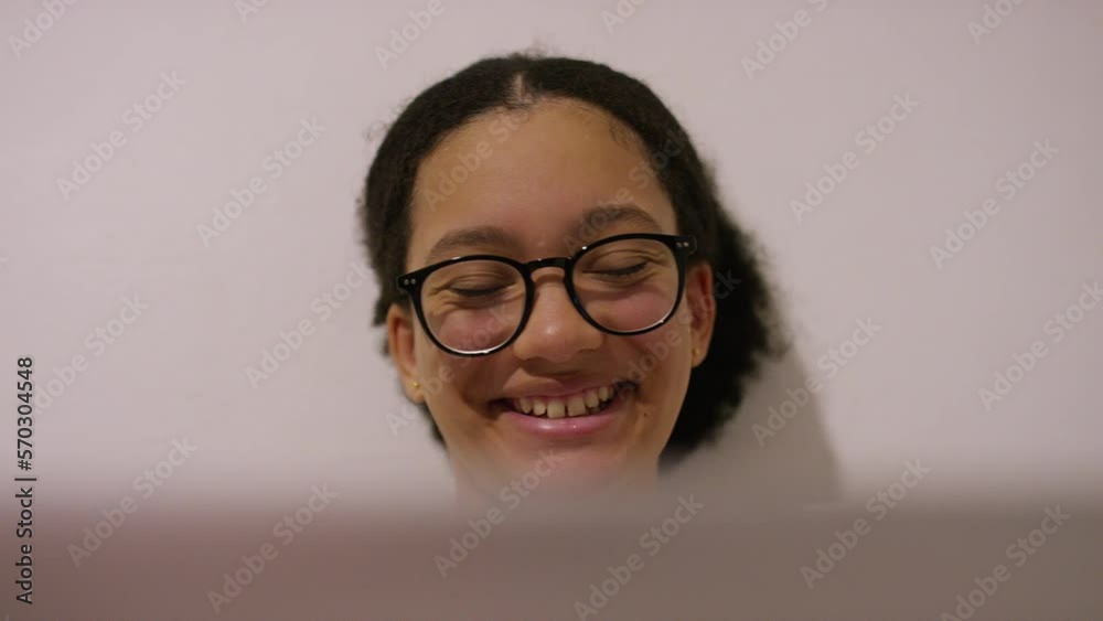 Handheld shot of young teenager smiling as she uses her laptop Handheld shot of young teenager smiling as she uses her laptop