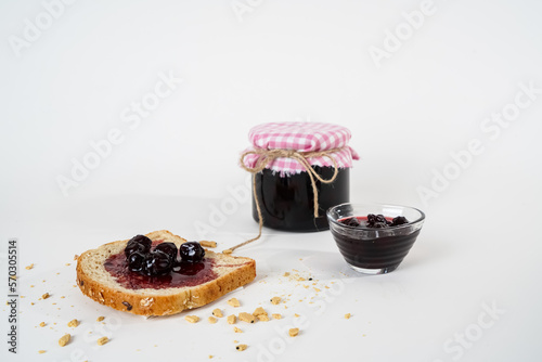 Homemade sour cherry jam, jar, small bowl and a slice of bread with jam isolated on white background.