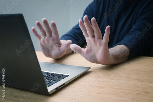 Hands in defensive gesture against a laptop computer, avoiding further work on a hacked system or other danger and offence, online risk in business and privacy, copy space,