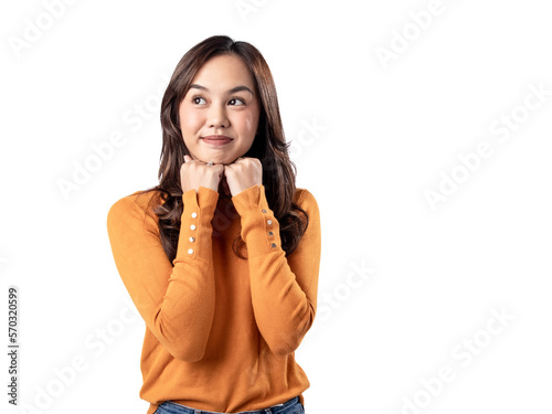 A portrait of a happy Asian Indonesian woman wearing an orange sweater and clenching both hands under her chin, isolated on a white background