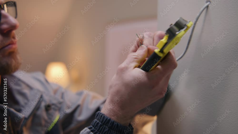 Close up shot of repairman in uniform and glasses works with cable twisted pair. Electrician removes insulation from wire with professional tool in the apartment. Installation of the Internet.