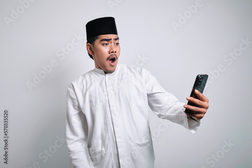 Asian muslim man in white clothes holding smartphone doing winning gesture holding mobile phone © Reza