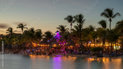 A tastefully lit beach bar, on a tropical beach next to the shore.  The colourful lights are reflecting in the sea. © parkerspics