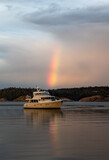 A beautiful rainbow in the sky lands right upon a yacht at a peaceful anchorage in the San Juan Islands of Washington State.