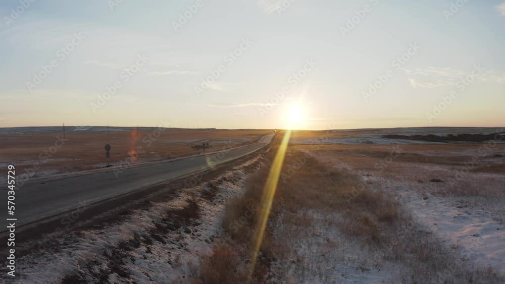 Empty road in the steppe covered with snow at dawn with cars in the distance Empty road in the steppe covered with snow at dawn with cars in the distance