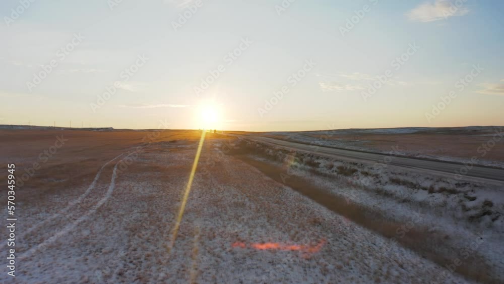 A white car drives along the road at dawn in the steppe covered with snow illuminated by the rays of the sun, front view, side view A white car drives along the road at dawn in the steppe covered with snow illuminated by the rays of the sun, front view, side view