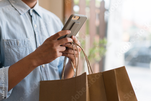 Close up of man`s hand holding smart phone research shopping mall and shopping bags while walking on the street.