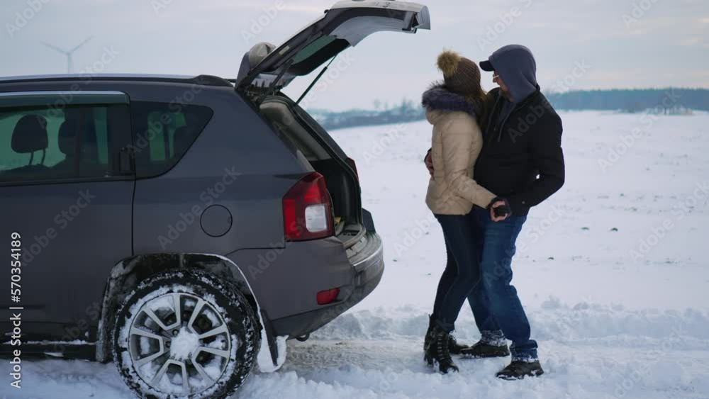 Funny dancing smiling hugging man and woman near open car trunk in snowy field. Family husband and wife activity on nature in cold winter season. Traveling journey and healthy active lifestyle concept Funny dancing smiling hugging man and woman near open car trunk in snowy field. Family husband and wife activity on nature in cold winter season. Traveling journey and healthy active lifestyle concept