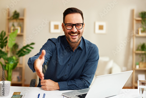 Handsome business man with a smile on his face is sitting at a desk and extending his hand for a handshake
