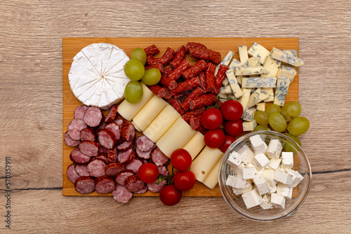 Wooden board with pieces of meat, feta cheese and vegetables, on the kitchen counter, top view.