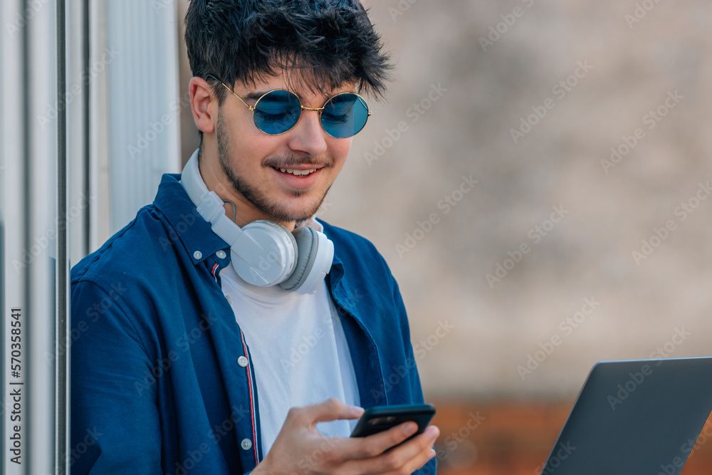 young man with mobile phone and laptop wearing sunglasses outdoors young man with mobile phone and laptop wearing sunglasses outdoors