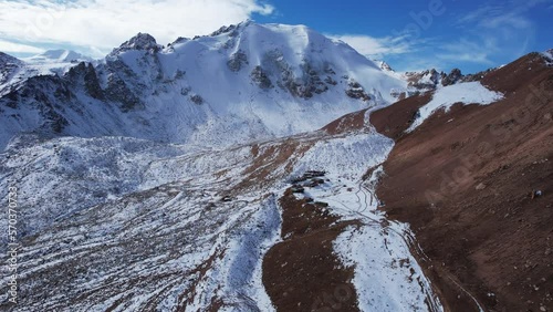 High snowy peaks and a small glaciological station. Drone view of the blue sky with clouds, steep cliffs and rocks. An ancient glacier covered with snow. Small houses are standing. Moraine lake photo