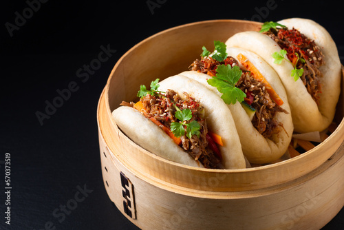 Food concept Homemade organic Pulled Beef Bao Buns or Gua Bao in bamboo stream tray on black background with copy space