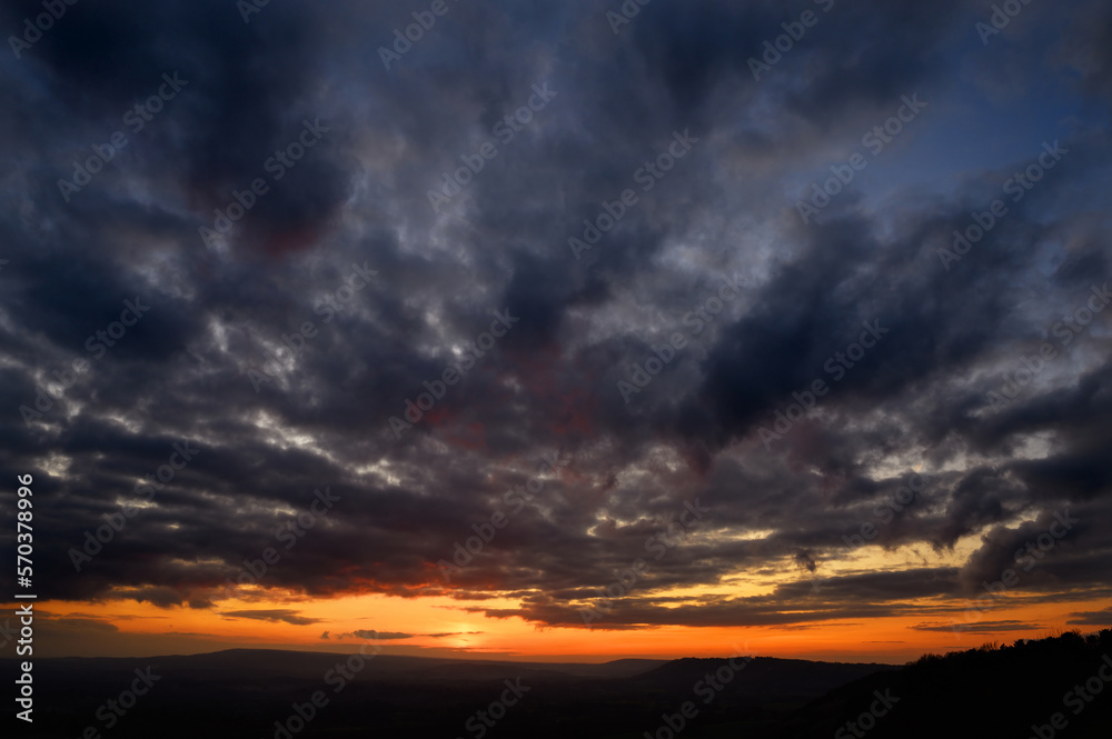 Dramatic sunset view from Colley Hill between Reigate and Dorking in Surrey, UK. Surrey Hills area of Outstanding Natural Beauty on the North Downs. Dark clouds, silhouette landscape and orange sky. Dramatic sunset view from Colley Hill between Reigate and Dorking in Surrey, UK. Surrey Hills area of Outstanding Natural Beauty on the North Downs. Dark clouds, silhouette landscape and orange sky.