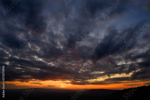Dramatic sunset view from Colley Hill between Reigate and Dorking in Surrey, UK. Surrey Hills area of Outstanding Natural Beauty on the North Downs. Dark clouds, silhouette landscape and orange sky.